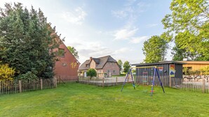 A residential backyard with a swing set, a brick house, and a wooden fence. - Gode Sünn vacation apartment in Tating for up to 4 people (Tating)