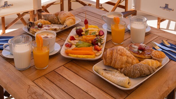 A table set with breakfast items, including croissants, fruit, and beverages, overlooking a coastal view with buildings and boats. - Relais del Mare (Sorrento)