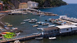 A coastal marina with boats docked, a pier, and buildings along the cliffside. - Relais del Mare (Sorrento)