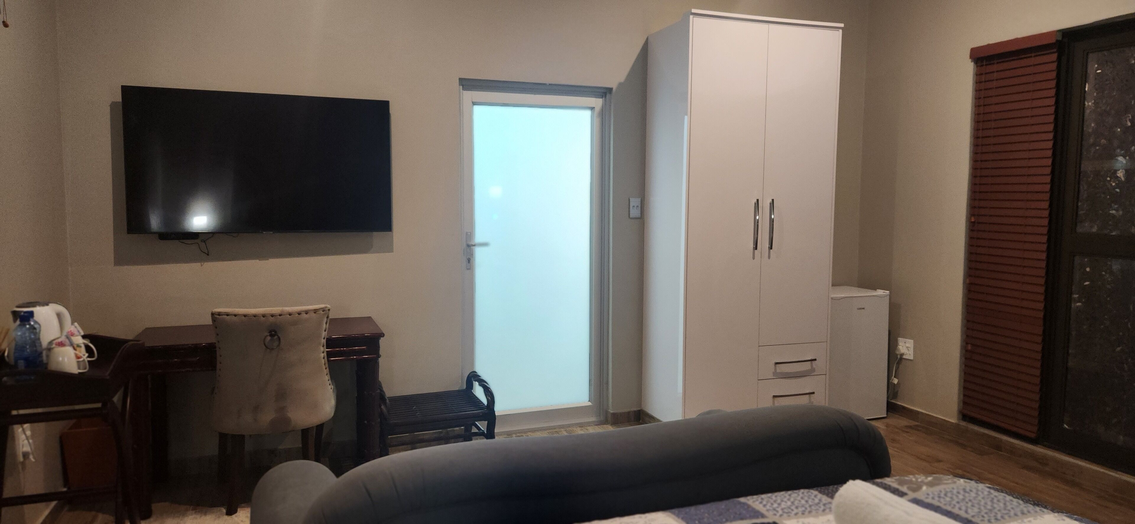 A bedroom with a bed, a desk, a chair, a wardrobe, a television, and a sliding door.