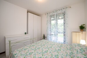 A bedroom with a bed, a dresser, a radiator, a window with curtains, and a plant. - Orchidea Apartment (Soiano del Lago)