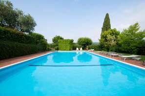 Uma piscina retangular com superfície azul translúcida, rodeada por um deck de tijolos e vegetação exuberante.