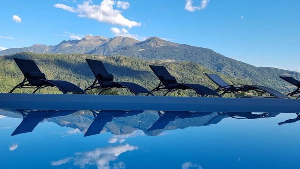 Una piscina a specchio con sedie a sdraio rivolte verso un paesaggio montuoso.