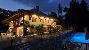 Una grande casa circondata da alberi, con piscina e un patio ben illuminato.