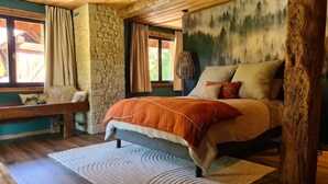 Una camera accogliente con parete in pietra, un letto con coperta arancione, una panca e un affresco raffigurante una foresta.
