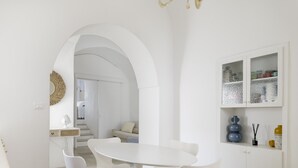 Un interior moderno con una mesa de comedor blanca, sillas blancas, un sofá y una escalera que conduce a otra habitación.