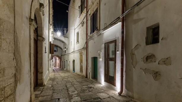 Un estrecho callejón adoquinado con paredes de piedra y arcos, que conduce a un edificio distante.