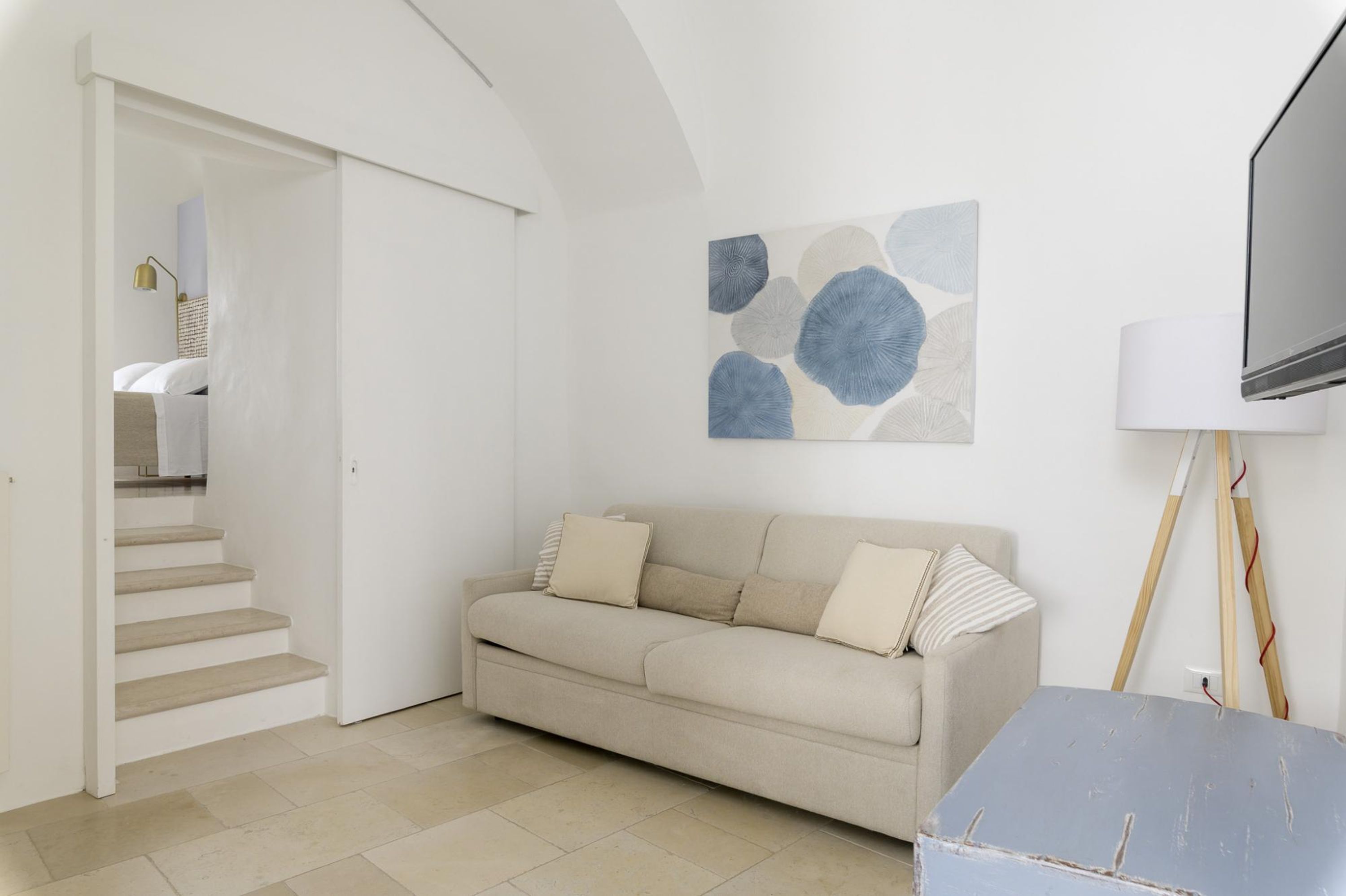 A living room with a sofa, a painting, a TV, and a lamp.
