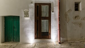 Un pasillo con una puerta verde, una puerta de madera con cortina, y una pared con pintura descascarada y un ventanal pequeño.