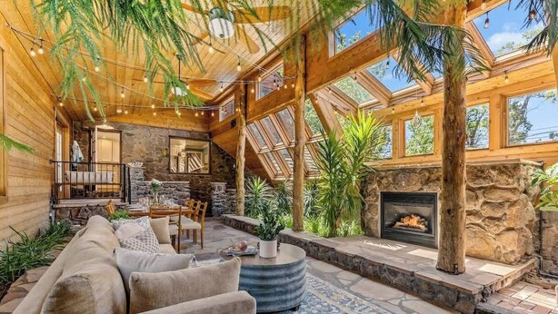 A cozy log cabin interior with a stone fireplace, wooden beams, and a stone fireplace surround. - Historic | Int Designed | DT Flag | Atrium | AC (Flagstaff)