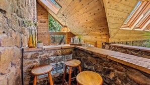 A rustic wooden interior with a stone wall, a wooden ceiling with skylights, and a bar area with stools. - Historic | Int Designed | DT Flag | Atrium | AC (Flagstaff)