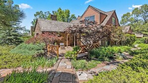 A rustic house with a stone pathway leading to a wooden deck, surrounded by lush greenery and trees. - Historic | Int Designed | DT Flag | Atrium | AC (Flagstaff)