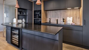 Cozinha moderna com armários escuros, uma ilha central, iluminação pendente e eletrodomésticos embutidos.