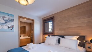 Quarto com uma cama grande, painéis de madeira, uma janela e um banheiro visível através de uma porta aberta.