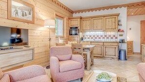Ett mysigt vardagsrum med en tv, rosa fåtöljer och en matplats med träskåp och en kakelbeklädd vägg bakom.