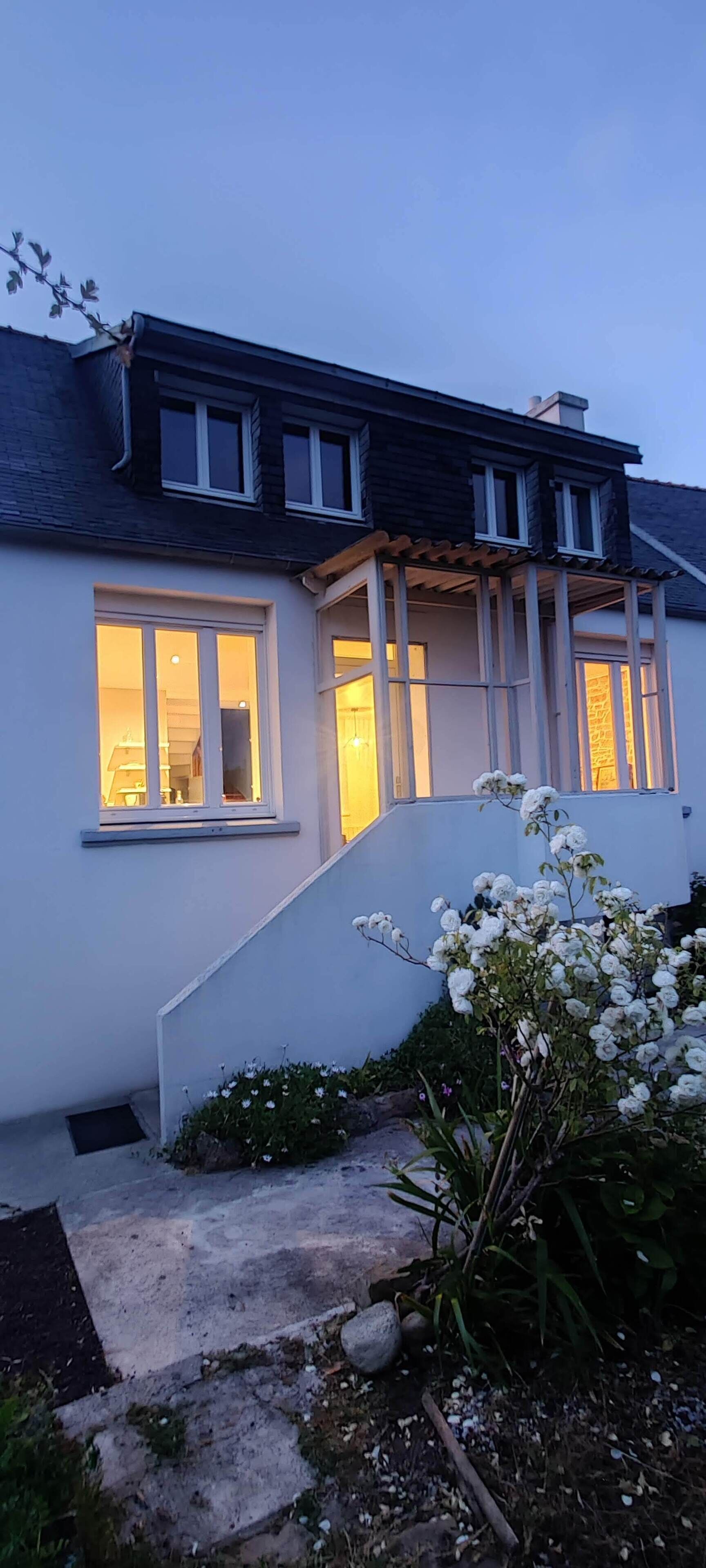 A house with a staircase leading to the entrance, a porch with a railing, and a garden with white flowers.