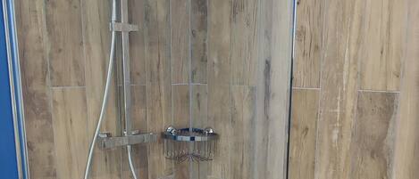 A glass-enclosed shower with a wooden panel wall, a white floor, and a blue accent wall.