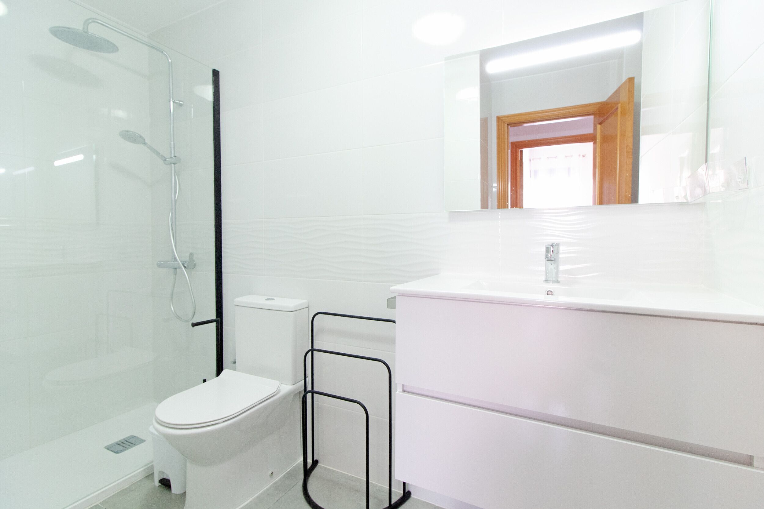 A modern bathroom with a glass-enclosed shower, a white toilet, and a vanity with a mirror.