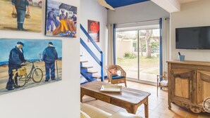Ein Wohnzimmer mit Holztisch, einer Couch, einem Fernseher und Kunstwerken an den Wänden.
