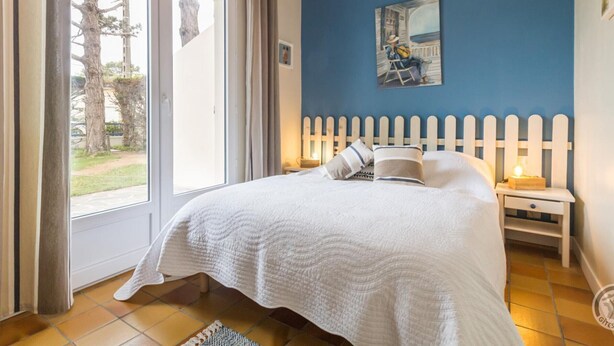 Ein Schlafzimmer mit Bett, Nachttisch, einem Gemälde und Blick durch eine Glastür.