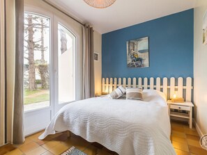 Quarto com cama, mesa de cabeceira, pintura e vista através de uma porta de vidro.
