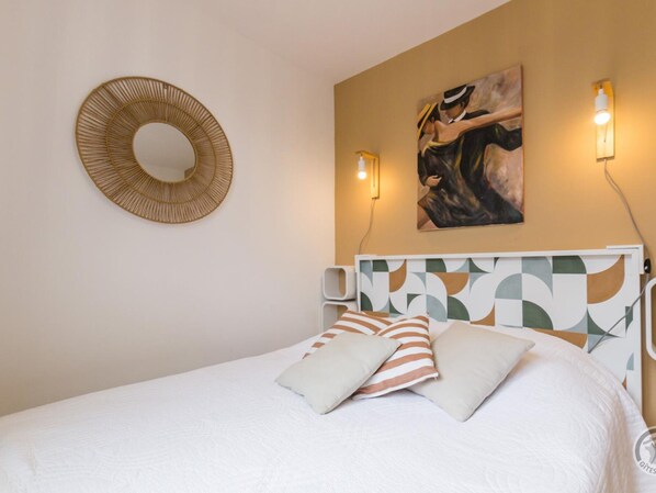 Une chambre à coucher avec un lit, un miroir rond, un tableau et deux lampes fixées au mur.