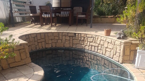 Una piscina con muros de piedra y un bordeado de baldosas.