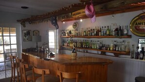 Zona de bar con taburetes de madera, estantes llenos de botellas de licores y un cartel con el horario del bar.
