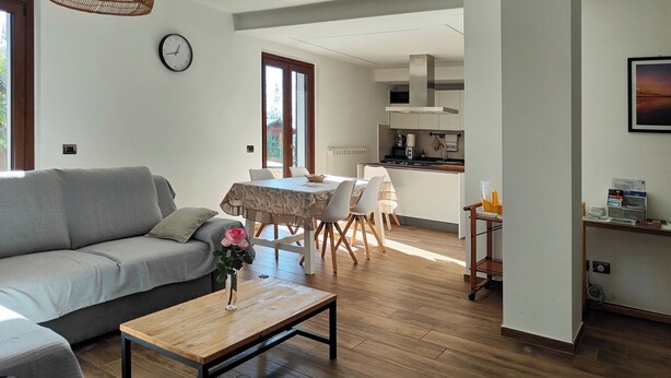 A modern living room with a grey sofa, a wooden coffee table with a vase, and a dining area with a table and chairs. - The house of roses (Passignano sul Trasimeno)