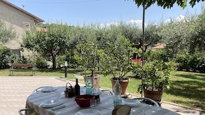 An outdoor dining table set with plates, glasses, and a bread basket, surrounded by potted plants and a bench in a garden setting. - The house of roses (Passignano sul Trasimeno)