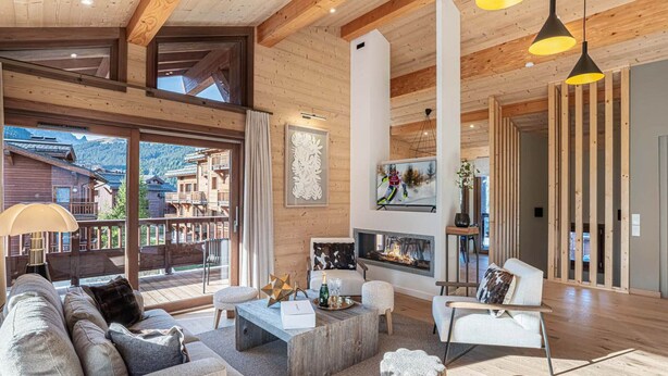 A spacious living room with a fireplace, wooden beams, and a large window overlooking a mountainous area.