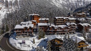 A snow-covered mountain resort with multiple wooden buildings, including lodges and a hotel, surrounded by dense forests and mountains.