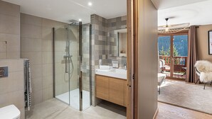 A modern bathroom with a glass-enclosed shower, a wooden vanity, and a view of a balcony with outdoor furniture.