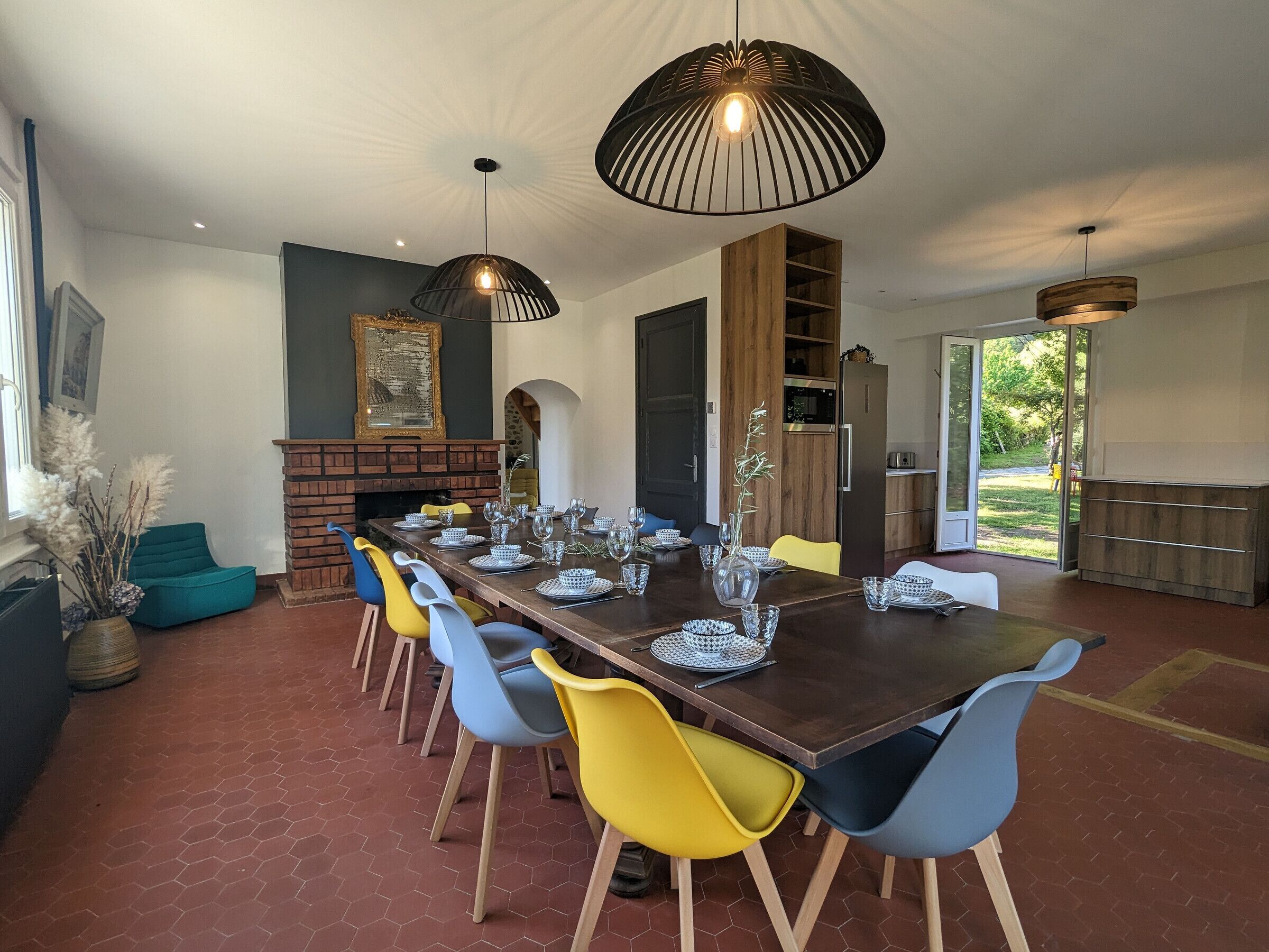 Een eetgedeelte met een lange tafel voor zes personen, omringd door kleurrijke stoelen, verlicht door moderne hanglampen.