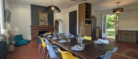 Een eetgedeelte met een lange tafel voor zes personen, omringd door kleurrijke stoelen, verlicht door moderne hanglampen.