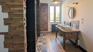 Un baño moderno con una pared de acento de piedra, un tocador de madera, un espejo grande y baldosas de suelo con diseño.