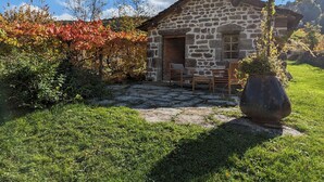 Un edificio de piedra con techo de piedra, un pequeño porche con dos sillas de madera y una planta grande en maceta.