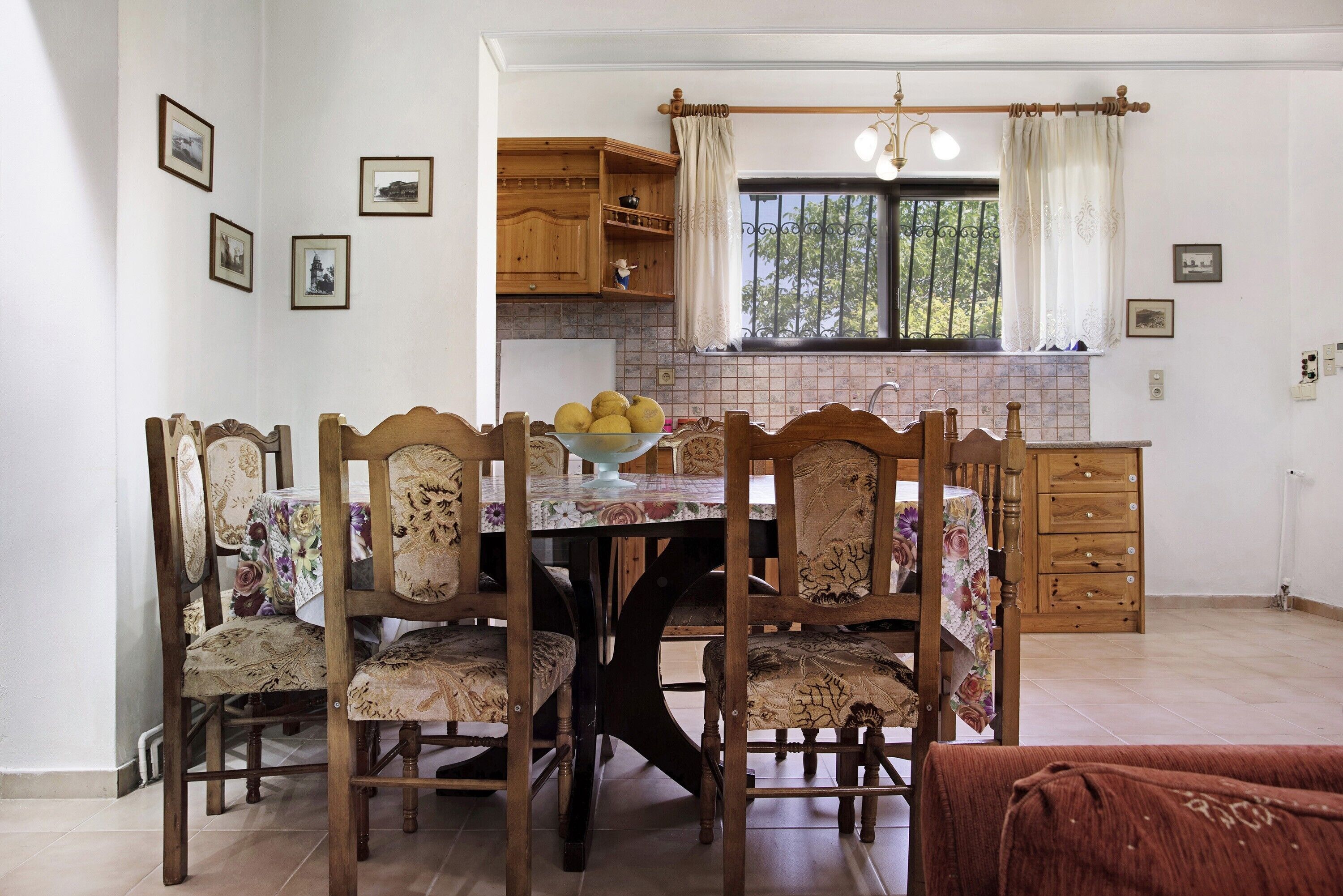 Un coin repas avec une table et des chaises en bois, une fenêtre avec des rideaux et, au fond, une cuisine.