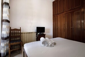 Een slaapkamer met een bed, een houten stoel, een televisie op een bijzettafeltje en een kledingkast.