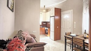 Ein Wohnzimmer mit einer Couch, einem Esstisch mit Stühlen, einer Küche im Hintergrund und einer Tür zu einem anderen Raum.