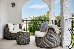 Ein Balkon mit Korbmöbeln, einer Lampe und Blick auf Gebäude und Grünflächen.