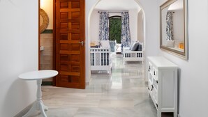 A hallway with a wooden door, a white table, a white console, and a view to a balcony with a white railing and a window with blue curtains. - Holiday Home 'Dalias' with Sea View, Wi-Fi and Air Conditioning (Nerja)