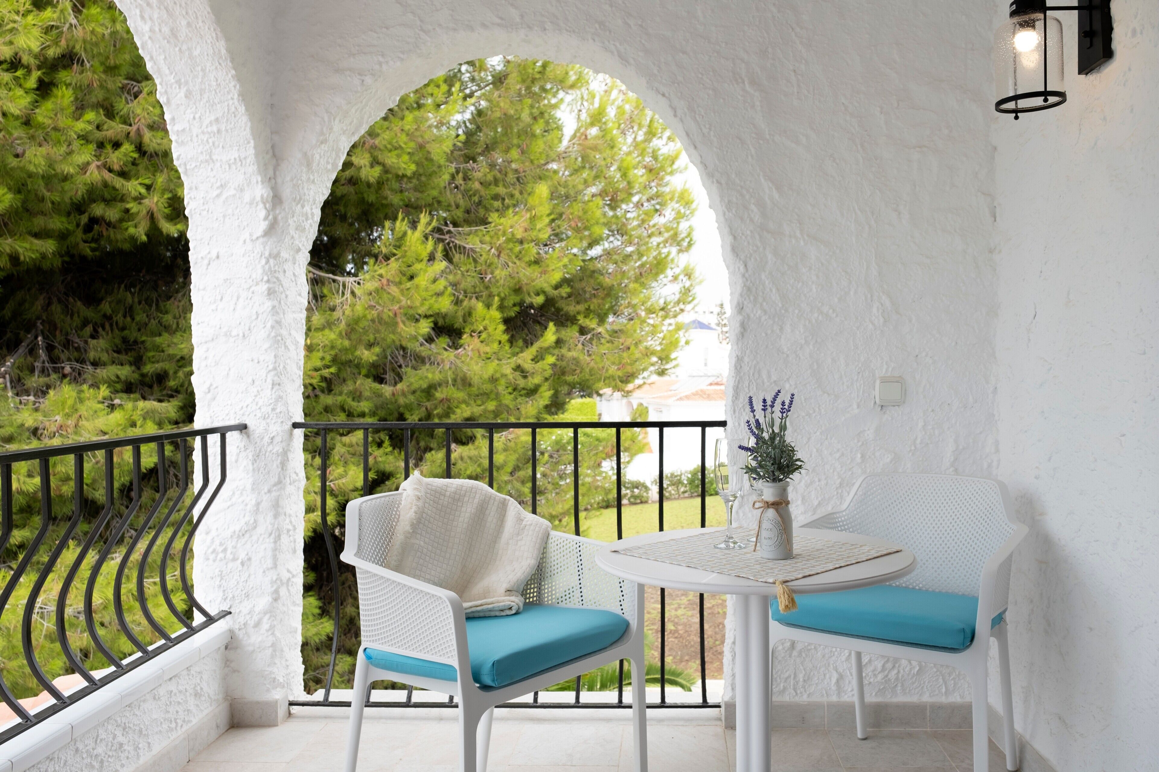 Ein Balkon mit weißen Wänden, einem runden Tisch, zwei Stühlen mit blauen Kissen und einem Blumentopf.