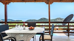 A covered outdoor dining area with a table set for two, a bottle, and a bowl of fruit. - Apartment 'Ventus Kalipso' with Sea View, Wi-Fi and Air Conditioning (Lefkada)