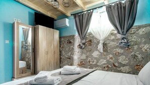 A bedroom with a bed, a wooden wardrobe, a mirror, and a stone-patterned wall. - Apartment 'Ventus Kalipso' with Sea View, Wi-Fi and Air Conditioning (Lefkada)