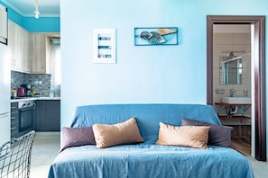 A bedroom with a bed, pillows, a wall-mounted artwork, a kitchen area, and a bathroom with a mirror.