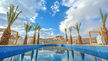 Une piscine d’un bleu éclatant, bordée de palmiers et surmontée de parasols blancs, qui reflète le ciel.