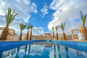 A clear blue pool with palm trees and white canopies, reflecting the sky. - Pearl Camp Agafay (Marrakech)