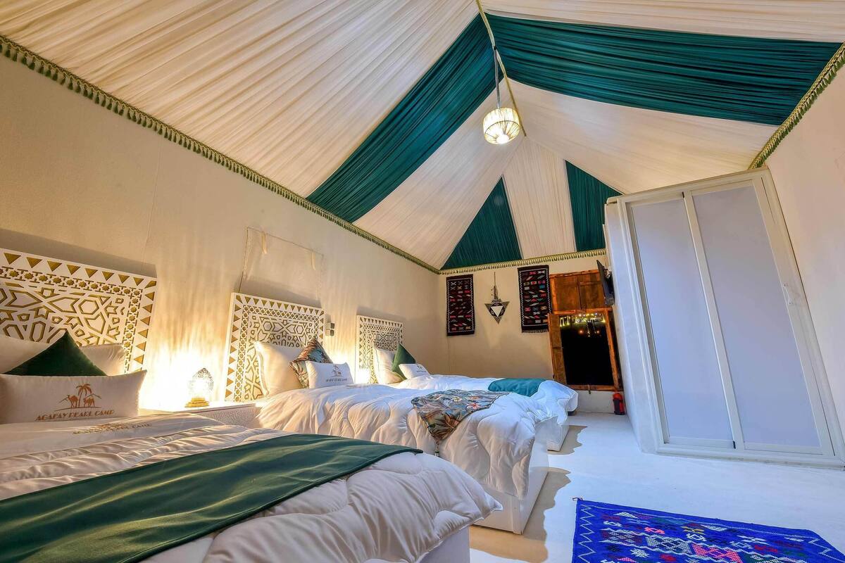 A tented room with two beds, patterned headboards, and a view of the night sky.