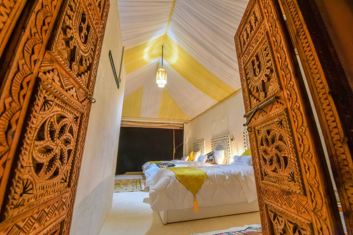 A room with a bed, a hanging light fixture, and intricate carved wooden doors.